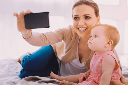 微笑的妇女手持智能手机拍照时与她的婴儿
