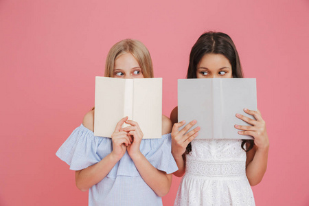 照片的兴奋或惊讶的欧洲女孩810 穿着礼服覆盖他们的脸与书籍隔绝粉红色背景