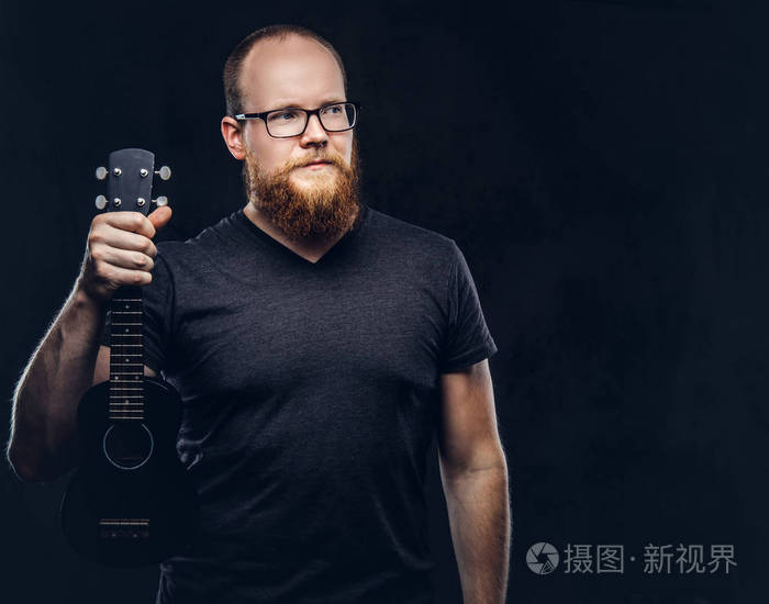 身穿灰色 t恤衫的红胡子男音乐家戴着四弦琴.在深色纹理背景下隔离
