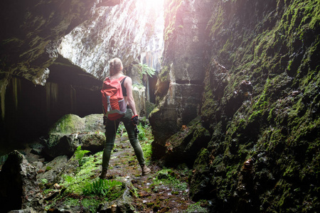 年轻妇女与橙色旅行背包和 lightern 探索古堡垒洞穴, 从后面看