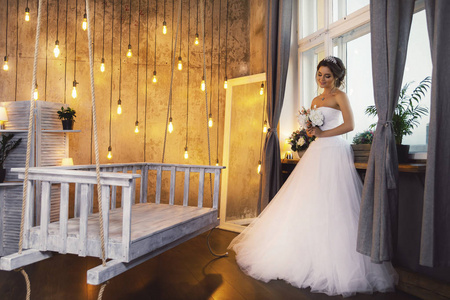 年轻快乐的新娘穿着漂亮的郁郁葱葱的礼服在房间里有很多灯泡