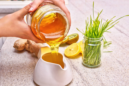 金色的液体有机蜂蜜从罐子里倒。绿色小麦 柠檬和姜一排毒果汁