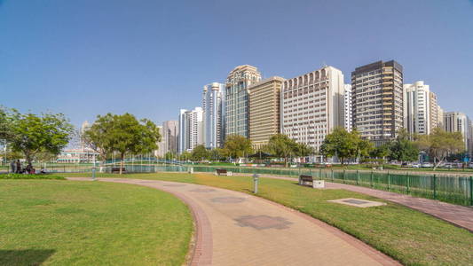 海滨大道海滨公园沿着阿布扎比的海岸线 timelapse hyperlapse 与摩天大楼的背景。从湖公园观看。树的一侧。晴天的