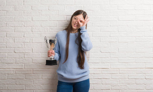 年轻的中国女子拿着奖杯微笑着做 ok 手势用手在眼睛看通过手指