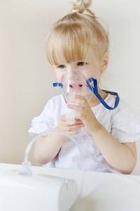小女孩在面具为吸入, 使吸入与喷雾器在家庭吸入器在桌, 室内, 生病的孩子