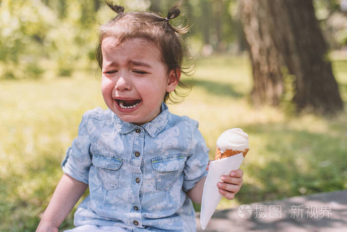 在公园里手里拿着冰淇淋锥的悲伤哭泣的孩子的肖像.小
