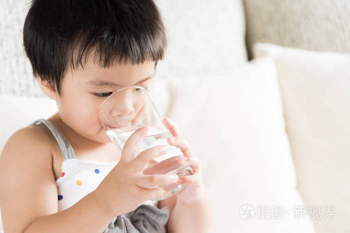 照片 可爱的小女孩在家里的沙发上喝水.医疗保健理念.jpg