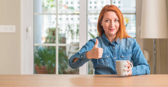 红头发的女人拿着一杯咖啡高兴地笑着做 ok 标志, 拇指与手指, 优秀的标志