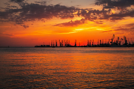 美丽的风景与火热的日落天空和海。日出时在海岸上的港湾。起重机的剪影反对火热, 橙色和红色天空