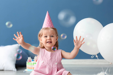 可爱的小女孩在生日聚会帽坐在地板室内