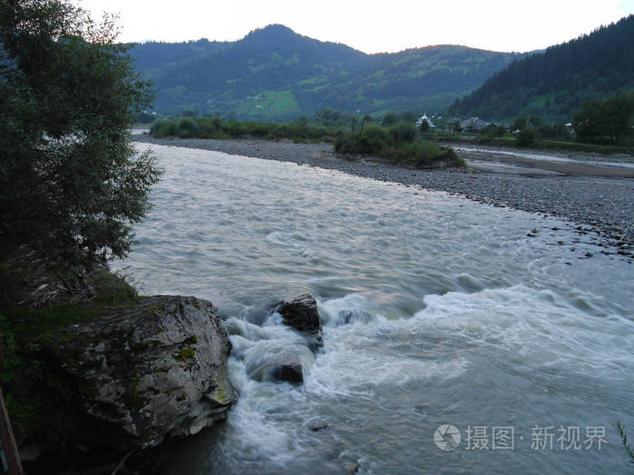 在大山脚下的乡村房屋的背景下, 快速, 湍急的河流流