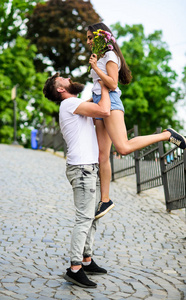 男的在养女朋友浪漫的约会散步。见到她很高兴。男人抱着女朋友的手, 而她拿着花花束在 l 浪漫的日期。情侣在恋爱会议的日期公园背景