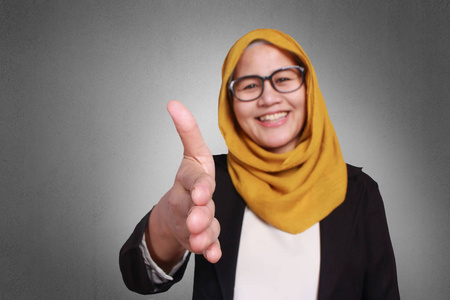 亚洲 muslimah 女商人戴着眼镜和西装, 带着友善的微笑, 想握手示意。在灰色上被隔离。关闭头部和肩部
