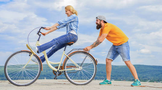 女人骑自行车的天空背景。女孩骑自行车, 而男人支持她。男人帮助保持平衡骑自行车。自行车服务。服务和协助。机修工帮助维修自行车。支