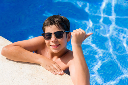 年轻的孩子在泳池边的海滩上指着拇指, 露出大拇指, 面带微笑