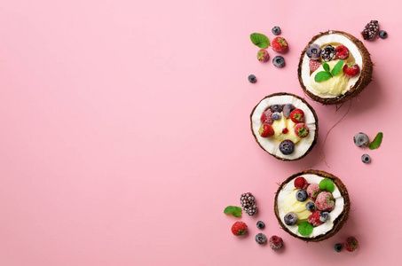 椰子冰淇淋与新鲜浆果在椰子一半粉红色背景与复制空间。顶部视图。流行艺术设计, 创意夏日概念。最小平放式食物