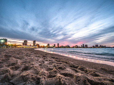 美丽的日落照片的沙滩作为波浪滚动从密歇根湖在北大道海滩在芝加哥与五颜六色的粉红色和蓝色的天空和灯光附近的海滩房子超越