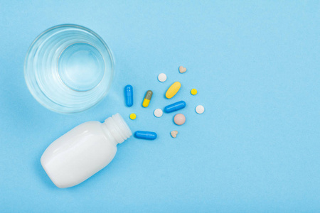 白色瓶与不同的药丸, 胶囊和水玻璃在蓝色背景与拷贝空间。使用药物预防和治疗疾病的概念