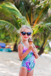 可爱的小女孩在冰激淋与棕榈树在海边沙滩上的太阳镜。天堂