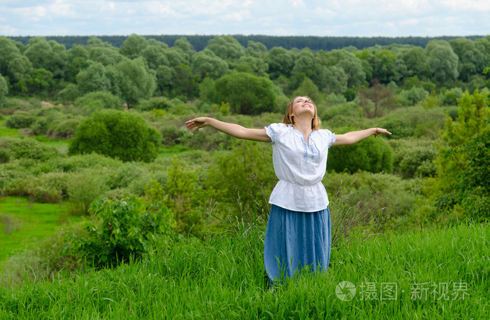 快乐的女孩站在背景场的灌木丛和抬头望着天空