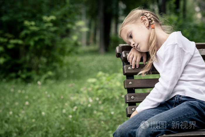 悲伤的金发小女孩坐在长凳上的肖像