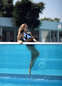 女孩摆在现代游泳池与明确的玻璃墙在度假胜地和水疗酒店。旅行和假期