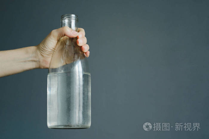 女人手拿瓶子与水在灰色墙壁背景与拷贝空间, 股票相片图片