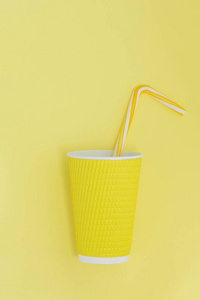 一个纸杯咖啡与鸡尾酒秸秆的抽象视图。黄色背景。相似的颜色