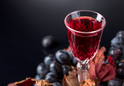 深色背景下的红葡萄酒水晶玻璃特写。带有干藤叶的深色葡萄。选择性焦点, 文本的可用空间