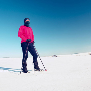 冬季旅游与雪鞋走在白雪皑皑的漂移。粉红运动夹克的徒步旅行者