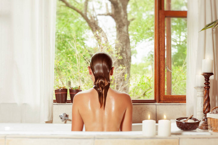 后视图的一个女人在浴缸里享受着水的过程, 浪漫的气氛中用蜡烛在浴室里的豪华水疗酒店, 美容和健康治疗 concep