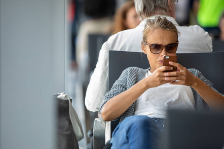 在国际机场登机口等候登机时使用手机的休闲金发年轻女子