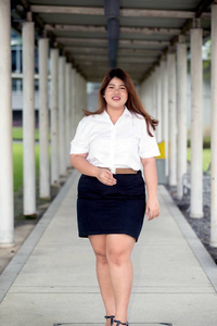 亚洲漂亮的笑脸脸胖女人在人行道上的学生制服姿势