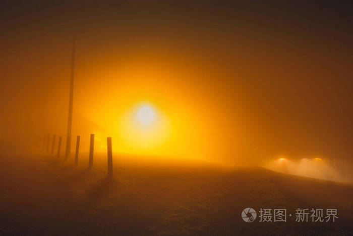 雾中的乡村街道在夜晚的橙色灯的路灯
