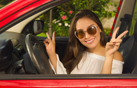 漂亮的女孩戴着墨镜和做胜利信号与她两只手在她红色的车