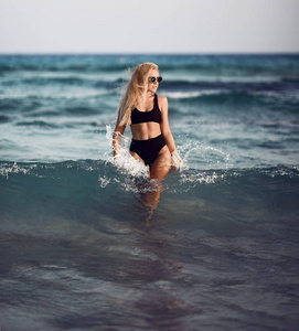 年轻美丽的女孩在海洋海水中摆出黑色的身体背心