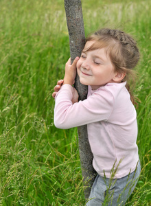 一个小微笑女孩，她的眼睛关闭拥抱一棵树干