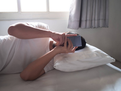年轻的亚裔男子, 手机智能手机躺在床上