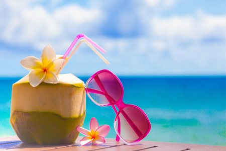 新鲜的椰子鸡尾酒和粉红色太阳镜上热带海滩的图片