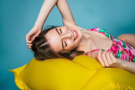 蓝色背景下躺在黄色气垫床垫上的微笑女孩肖像