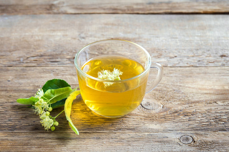 健康草本椴茶与一束新鲜的椴花在木质背景。杯有机椴茶, 草药饮料
