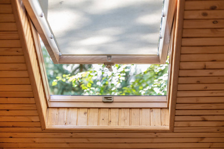 打开屋顶窗, 窗帘或窗帘在木屋阁楼。房间与倾斜天花板由自然生态材料和公园看法通过被打开的窗口。环境友好的房子