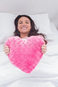 女人躺在床上，手里拿着一个毛茸茸的心垫