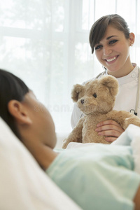 微笑的女医生给躺在病床上的女病人一只泰迪熊