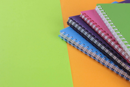 一叠五颜六色的笔记本在一个明亮的绿色和橙色背景。文具。与地方为题字