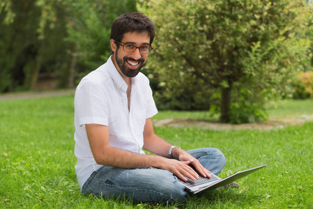 公园里的年轻人坐在草地上用笔记本电脑