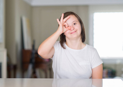 妇女在家与愉快的面孔微笑做 ok 标志用手在眼睛看通过手指