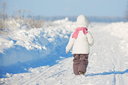 小女生的背观穿暖和的冬衣, 在严寒的冬天漫步, 喜欢户外玩耍, 享受阳光明媚的冬日, 摆在镜头前。童年和季节概念