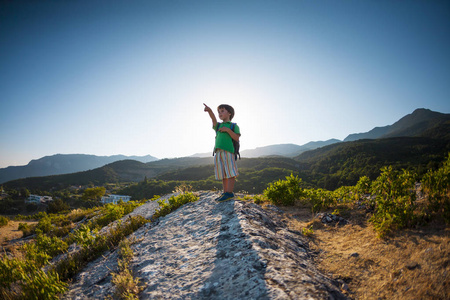 男孩在山顶的日落。有背包的孩子旅行到有趣的地方。那孩子沿着山路走。活动假期。一个小旅行者。爬