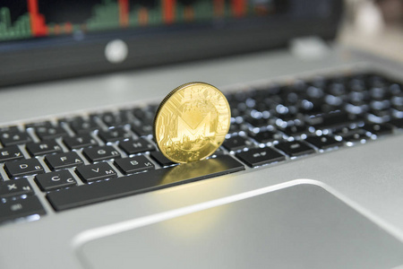 Monero 的金币在银色笔记本电脑的黑色键盘和图表图表在屏幕作为背景。Cryptocurrency 概念。ethereums 